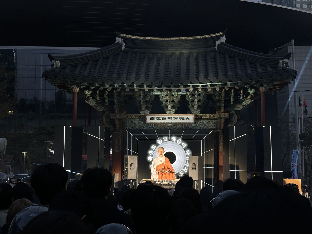A monk chants the Heart Sutra under flashing strobe lights at Bongeunsa, as animated Buddhist quotes circle across a digital backdrop. (Tammy Park/The Korea Herald)
