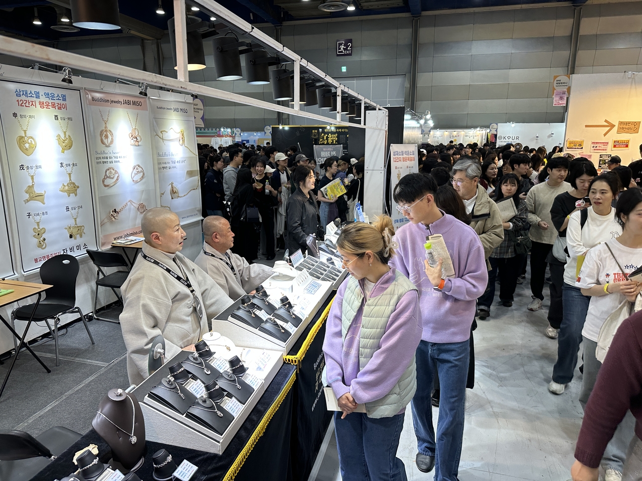 Rhythm, Faith, and Technology: 250,000 Attend Buddhism Expo, Driven by Gen Z Enthusiasm 20 Ven. Ilseo (right, background) observes visitors from his booth, which features Buddhist jewelry at the 2026 Seoul International Buddhism Expo. (Tammy Park/The Korea Herald)