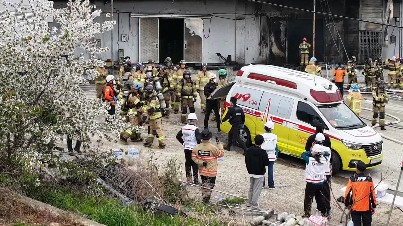 Firefighters watch as their colleague is carried to an ambulance. Two firefighters died in the blaze. (Yonhap)
