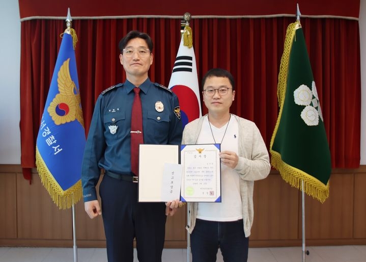 In this photo distributed by the Daegu Seongseo Police Station, a man who filed a report for a suspected romance scam case (right) receives a certificate of appreciation from police. (Daegu Seongseo Police Station)