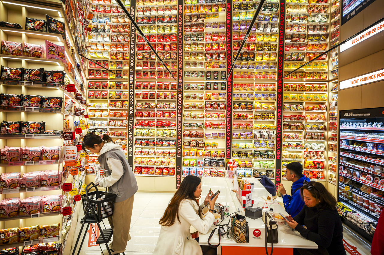 Visitors eat instant noodles beside a wall of ramyeon products at Emart24’s K-Food Lab in Myeong-dong on April 3. (Newsis)