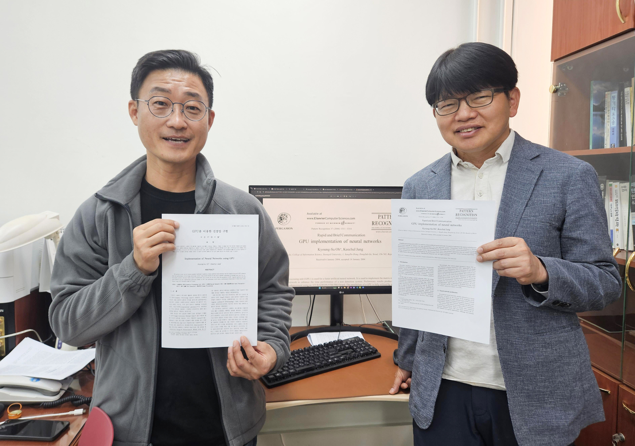 Professors Jung Kee-chul (left) and Oh Kyoung-su of Soongsil University hold up copies of their 2004 study "Implementation of Neural Networks using," which is considered to have contributed to advancement of modern artificial intelligence by finding application of graphics processing unit in faster artificial neural network. (Yonhap)