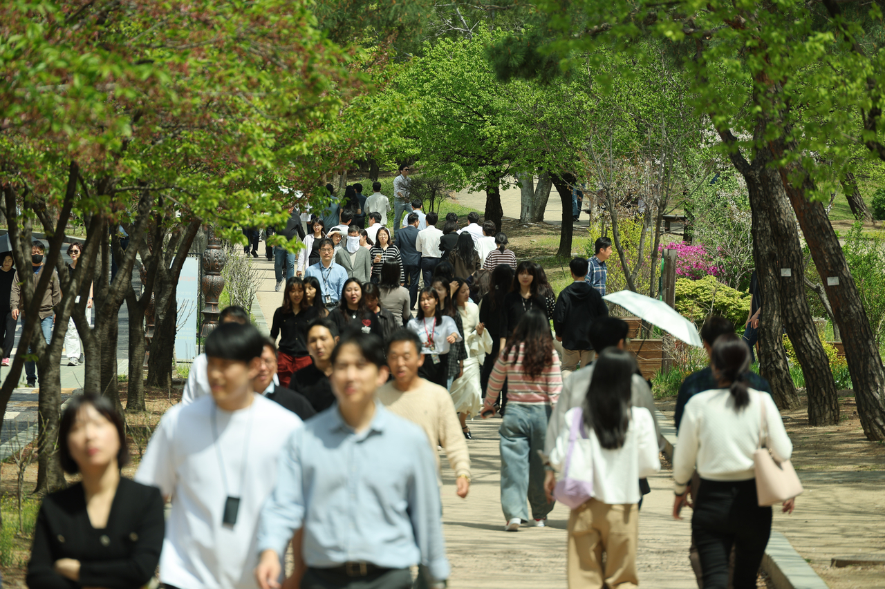 People stroll in light clothing under the sun at Yeoido Park earlier Thursday, with some already shading themselves with parasols. (Yonhap)