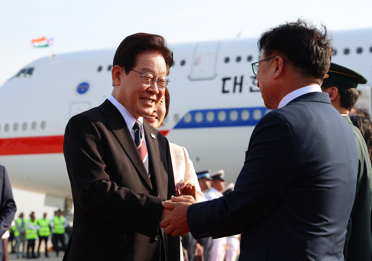 President Lee Jae Myung (left) shakes hands with an Indian official upon arrival at Palam Air Base in New Delhi on Sunday ahead of a summit with Indian Prime Minister Narendra Modi. (Yonhap)