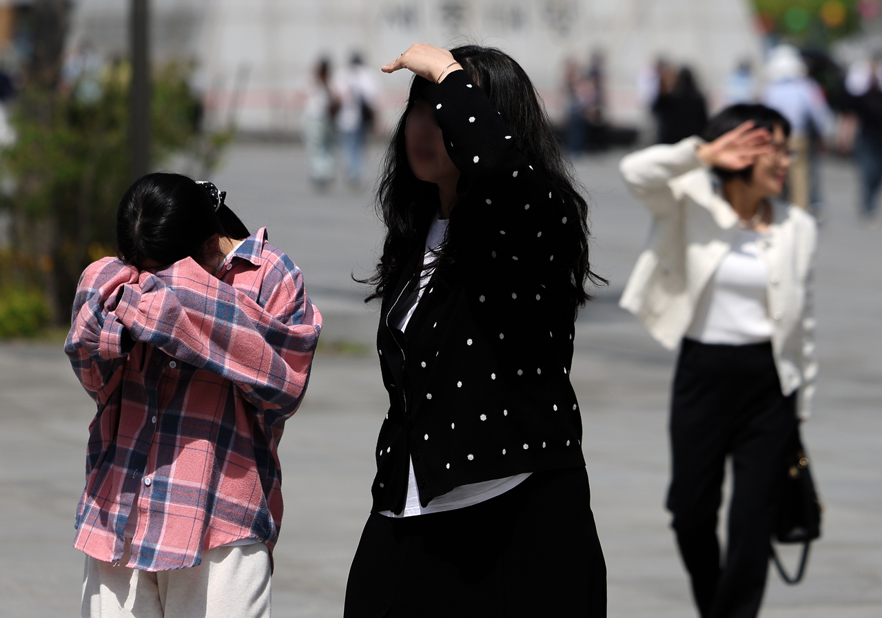 Pedestrians shield themselves from the sun as they walk through Gwanghwamun Square in Seoul on Sunday. (Newsis)