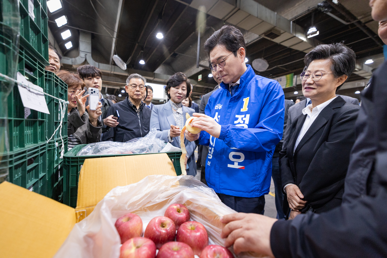 Chung Won-o (second from right) peels an apple during a visit to the agricultural products market in Songpa-gu, Seoul, Friday. (Yonhap)