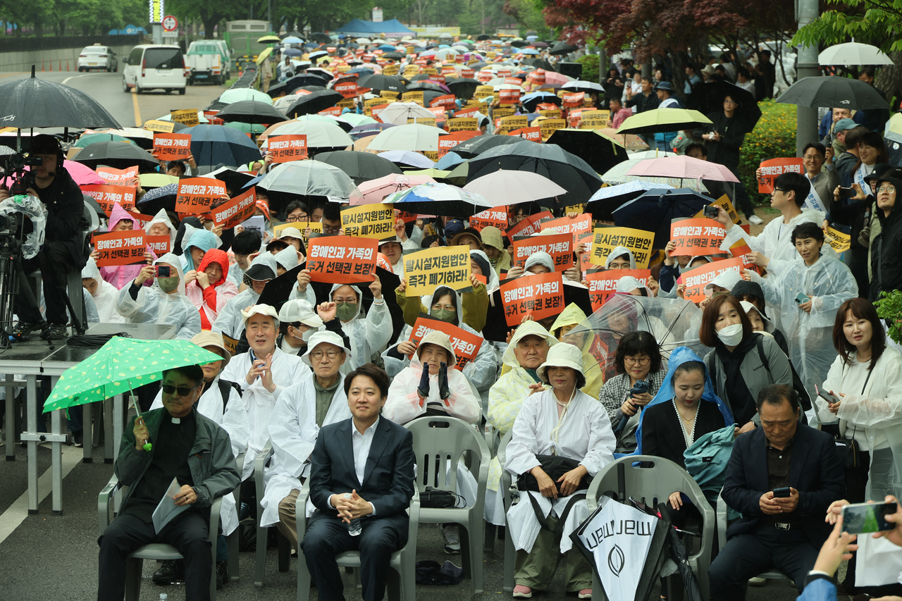 The Parents’ Association of Residents with Disabilities and facility operators hold a protest on Monday in front of the National Assembly, with Lee Jun-seok (second from left, front row) of the minor opposition Reform Party attending. (Yonhap)
