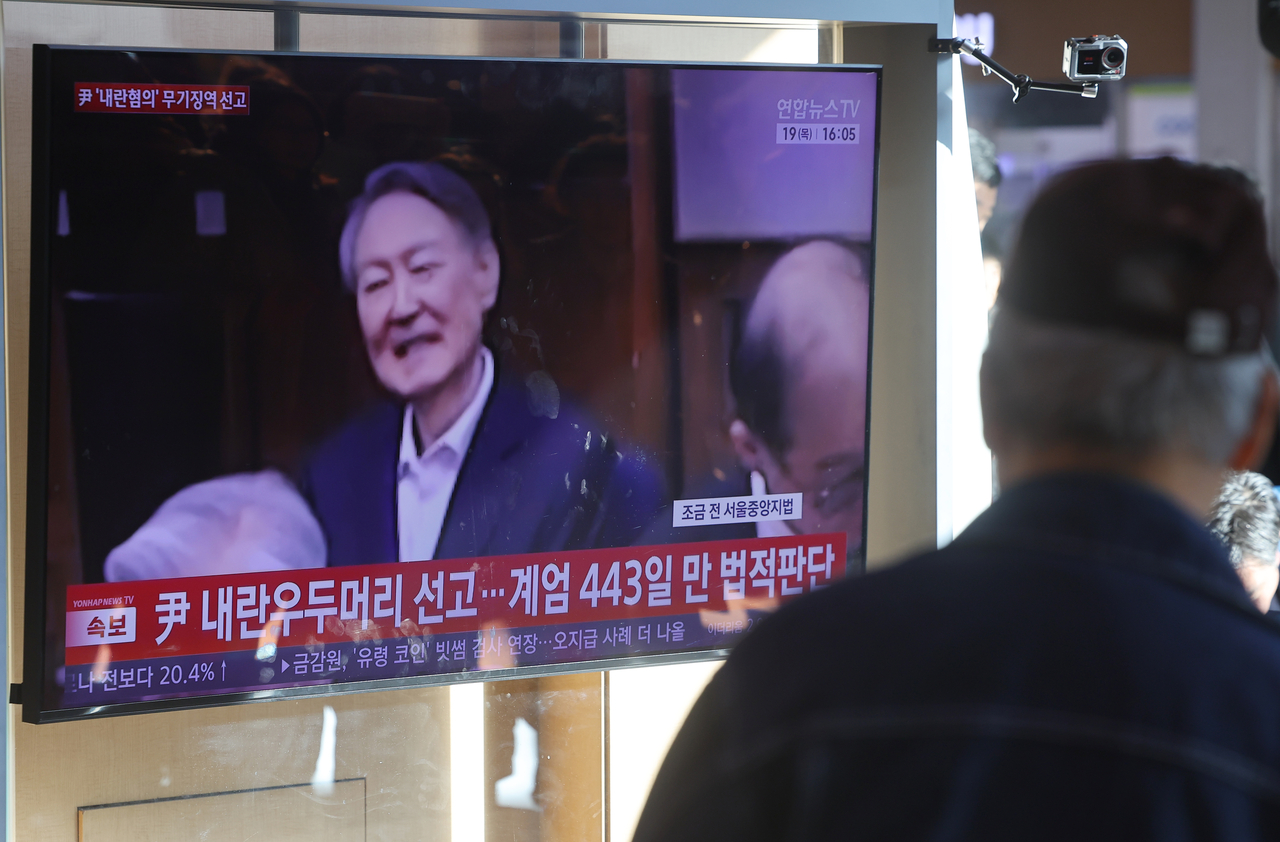 This file photo, taken Feb. 19, 2026, shows a person watching a news report of former President Yoon Suk Yeol's conviction on charges of leading an insurrection through his failed 2024 martial law bid aired in a live broadcast at Seoul Station in central Seoul. (Yonhap)