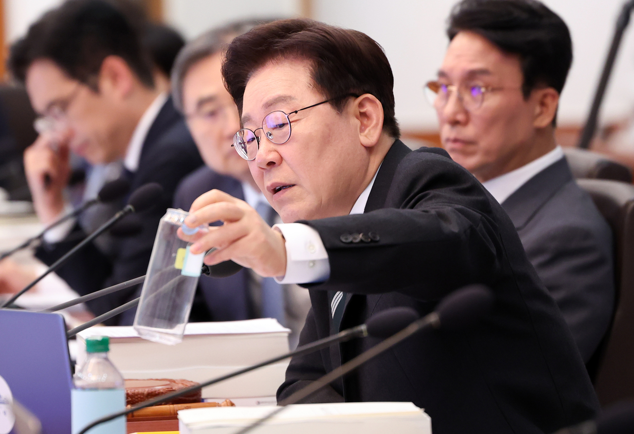 President Lee Jae Myung (center) asks about the recyclability of a plastic bottle with an aluminum cap during a meeting with Environment Minister Kim Sung-hwan at Cheong Wa Dae in Seoul on Tuesday. (Yonhap)