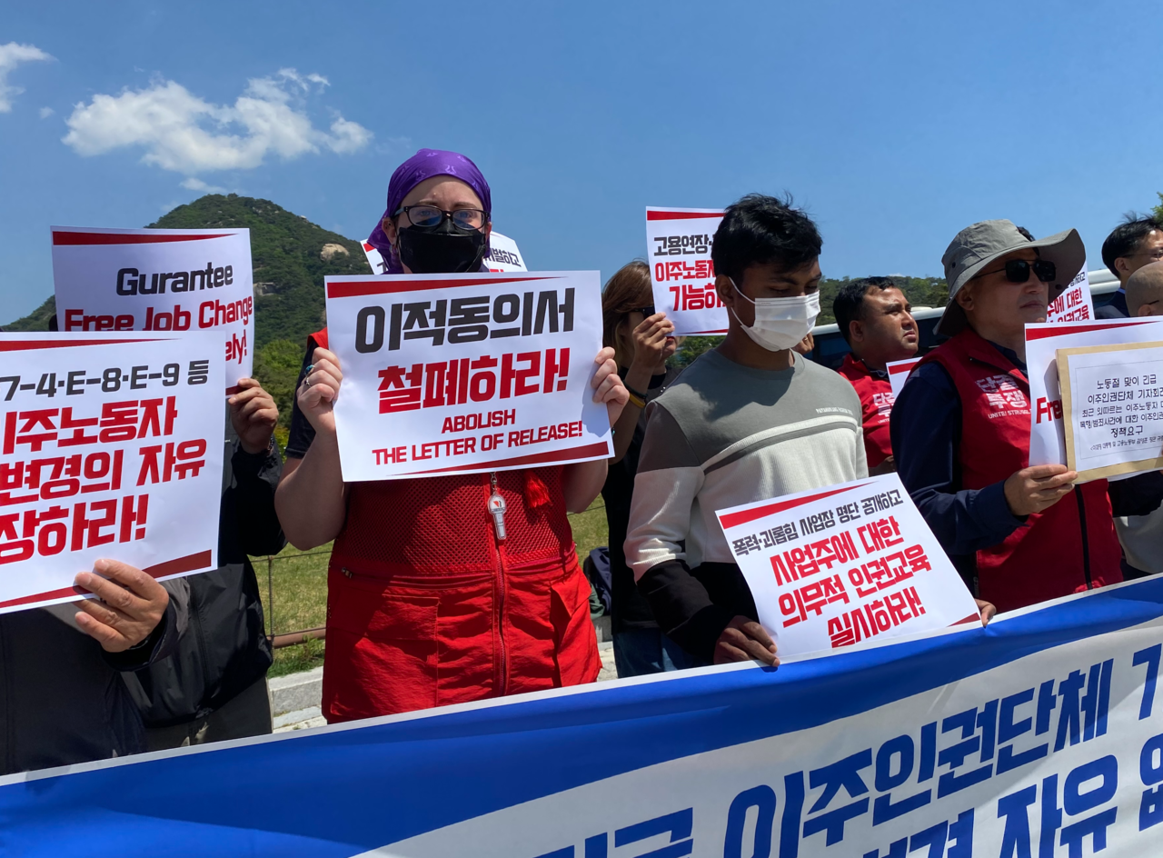 Erin Day (left), chair of the Seoul Native Language Teachers Union, and Rakibul Islam (center), a Bangladeshi worker, hold signs calling for stronger human rights protections for foreign workers in Korea during a press conference Thursday in front of Cheong Wa Dae in central Seoul. (Lim Jae-seong/The Korea Herald)