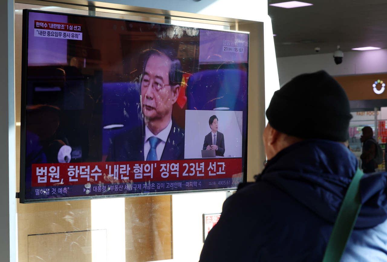 Passerbys watch news coverage at the Seoul Station waiting lounge on Jan. 21, regarding the first-trial sentencing of former Prime Minister Han Duck-soo. (Newsis)