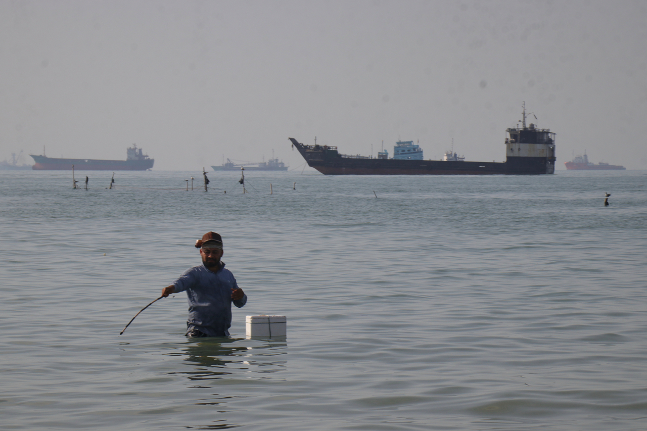 A man appearing to fish stands in the water as bulk carriers, cargo ships and service vessels line the horizon in the Strait of Hormuz off Bandar Abbas, Iran, Monday, April 27. (AP)