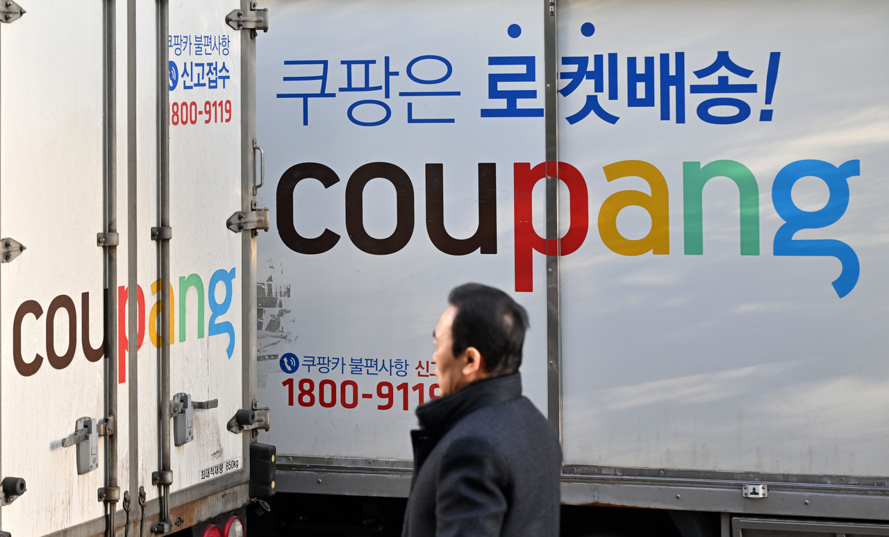 A pedestrian walks past Coupang delivery trucks at a Coupang logistics center in Seoul on Feb. 6. (Im Se-jun/The Korea Herald)