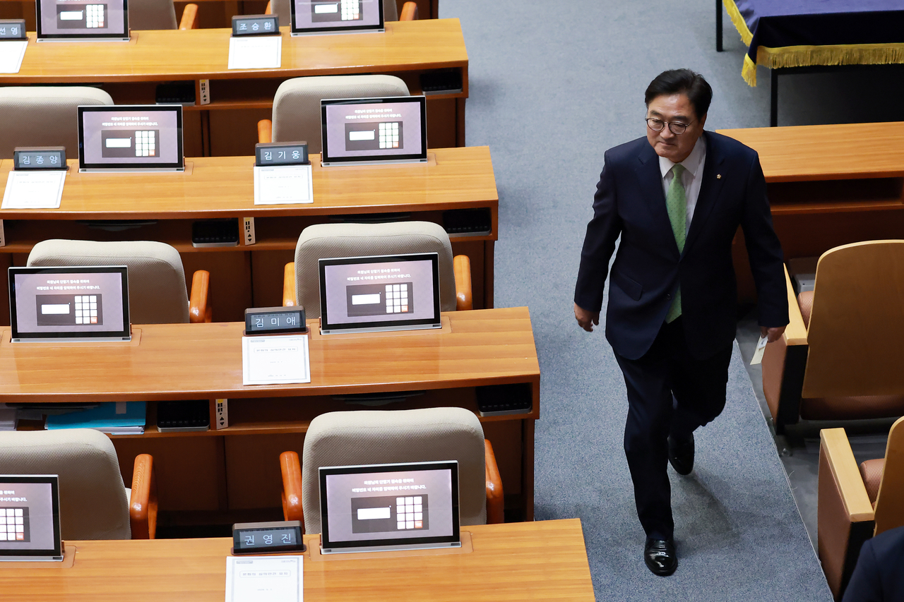 National Assembly Speaker Rep. Woo Won-shik walks along an aisle in the main chamber of the National Assembly on Thursday, as he passes seats left by People Power Party's lawmakers. (Yonhap)