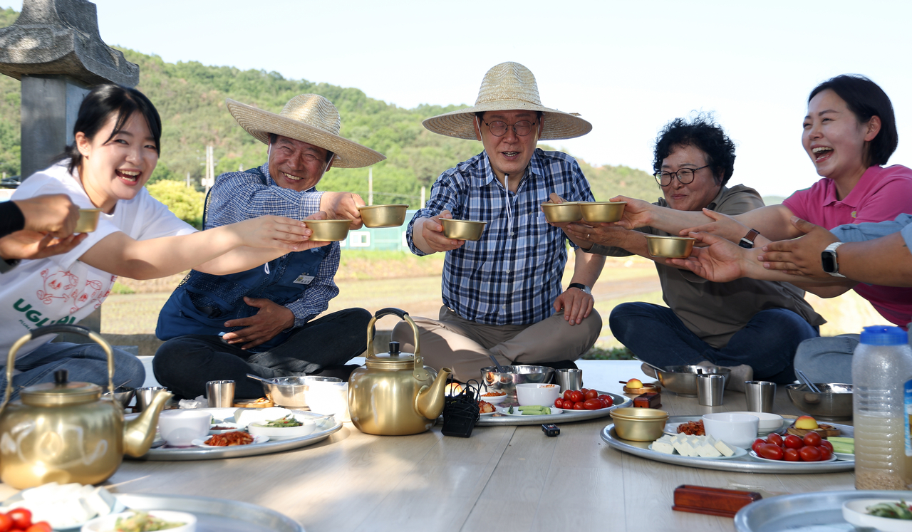 South Korean President Lee Jae Myung toasts with residents while sharing “saecham,” a traditional farm break meal, at a rice planting site in Sobo Myeon, Gunwi County, Daegu, Friday. (Yonhap)