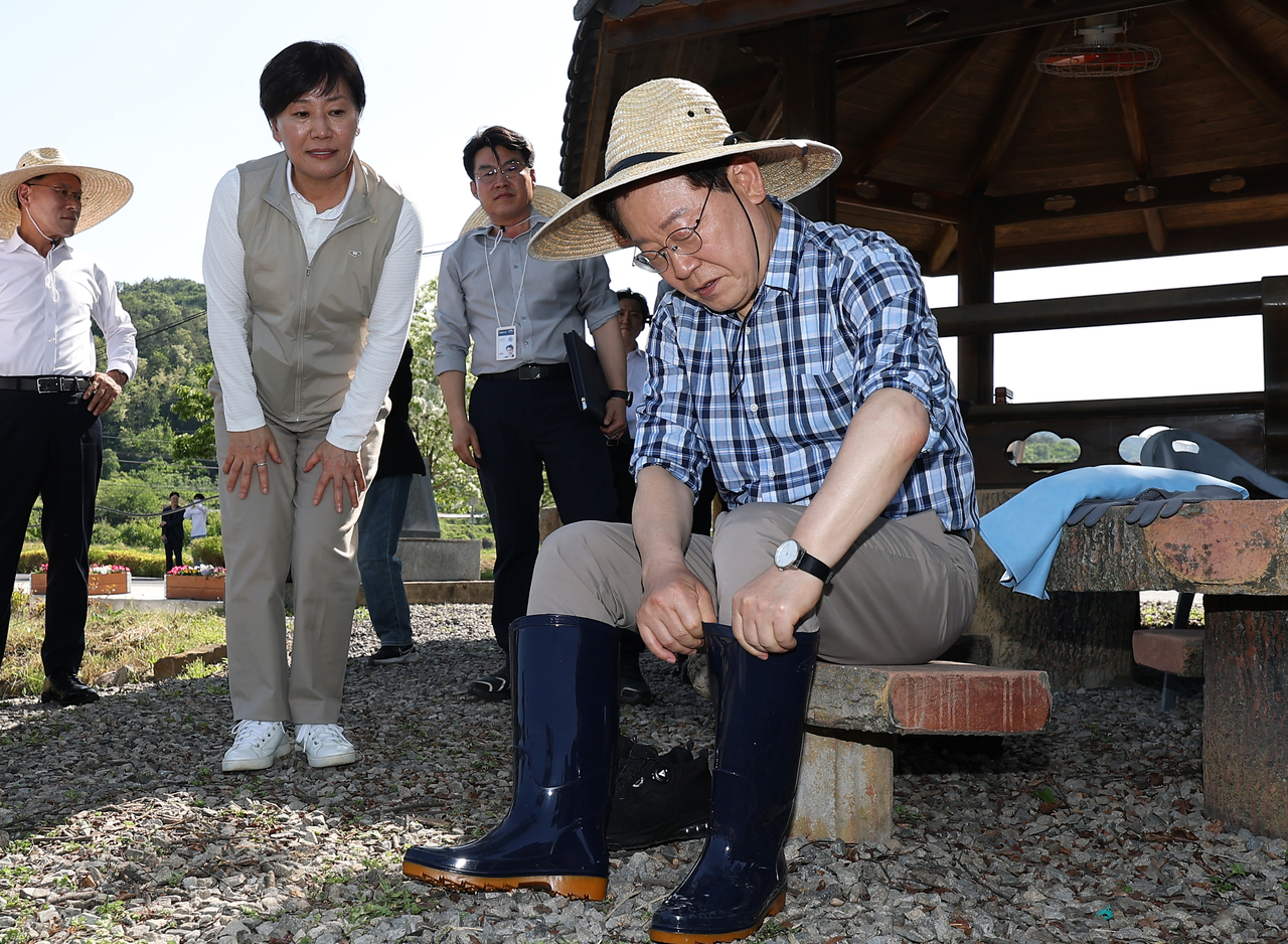 South Korean President Lee Jae Myung puts on rubber boots before a rice planting in Sobo Myeon, Gunwi County, Daegu, Friday. (Yonhap)