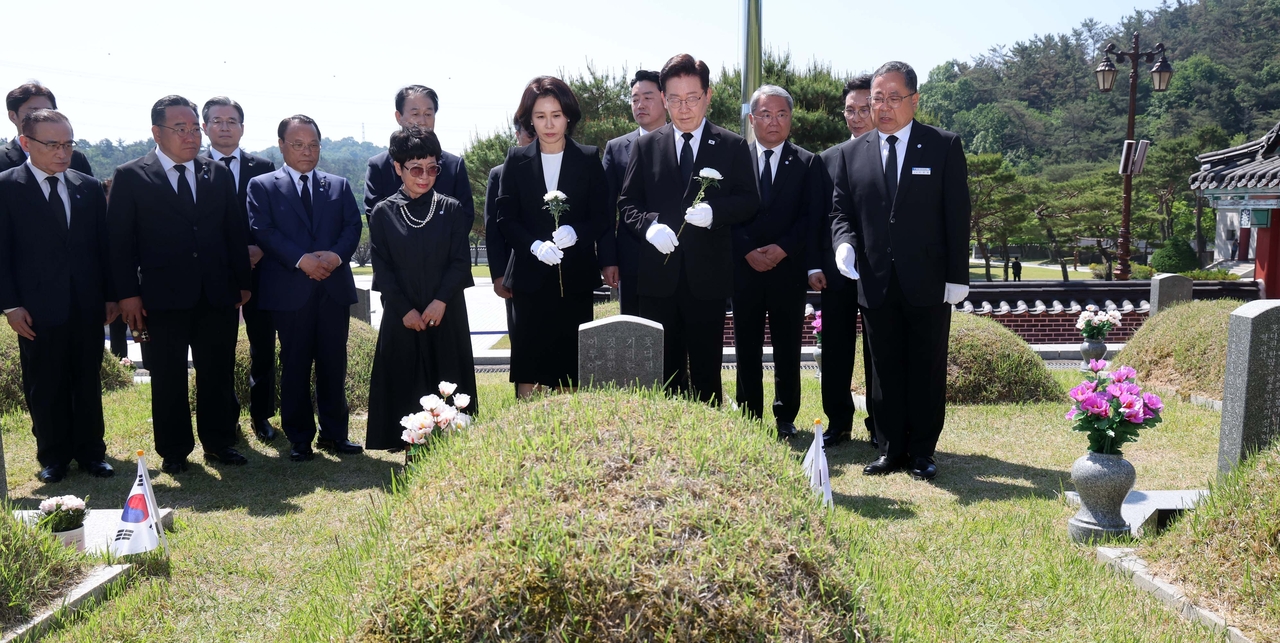 President Lee Jae Myung (right, front), alongside his wife, Kim Hea Kyung (left, front), offers a flower as he visits the tomb of Park In-bae, a late pro-democracy fighter, at a national cemetery for slain pro-democracy fighters in Gwangju on Monday, the 46th anniversary of a pro-democracy uprising. (Pool photo via Yonhap)