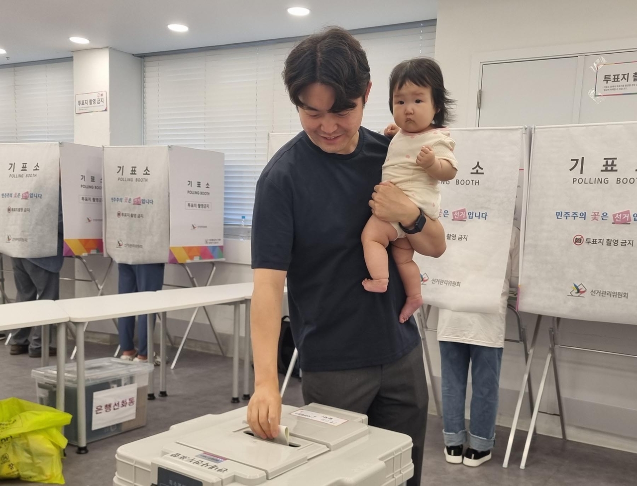 A voter carrying a toddler casts a ballot at a polling station in Daejeon on Friday. (Yonhap)