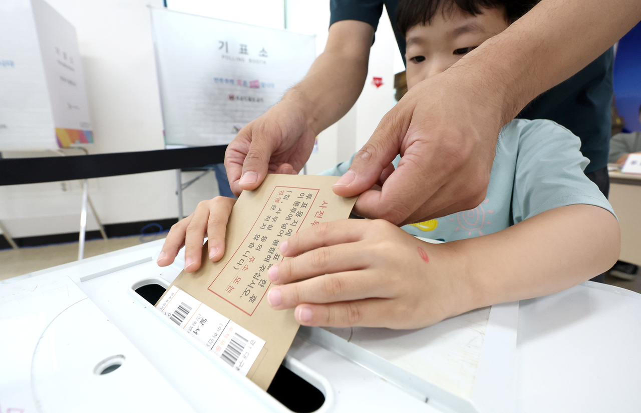 A boy helps insert a ballot into a ballot box alongside a voter at a polling station in Daegu on Friday. (Yonhap)