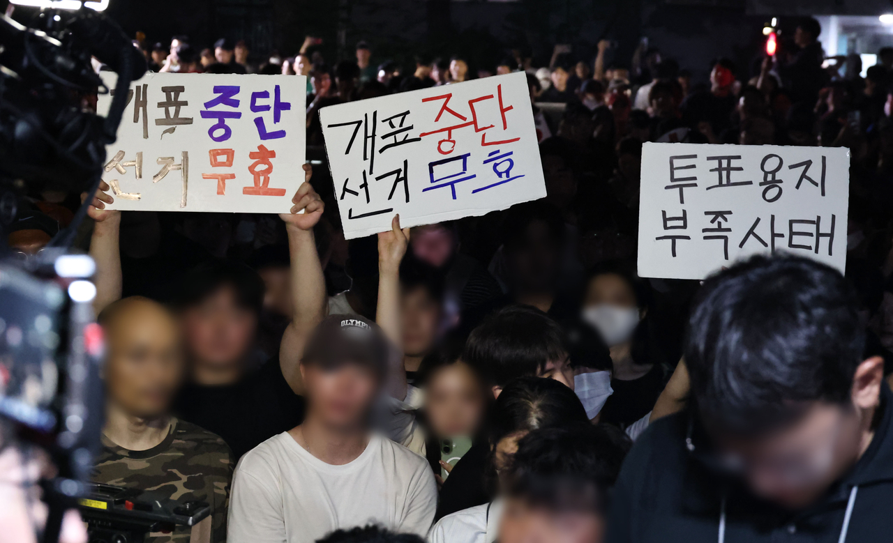 People gather outside the No. 2 polling station in Jamsil 7-dong, Songpa-gu, Seoul, Wednesday, holding signs reading "Suspend vote counting" and "Invalidate the election" after voting hours were extended to 10 p.m. due to a ballot shortage during the June 3 local elections. (Yonhap)