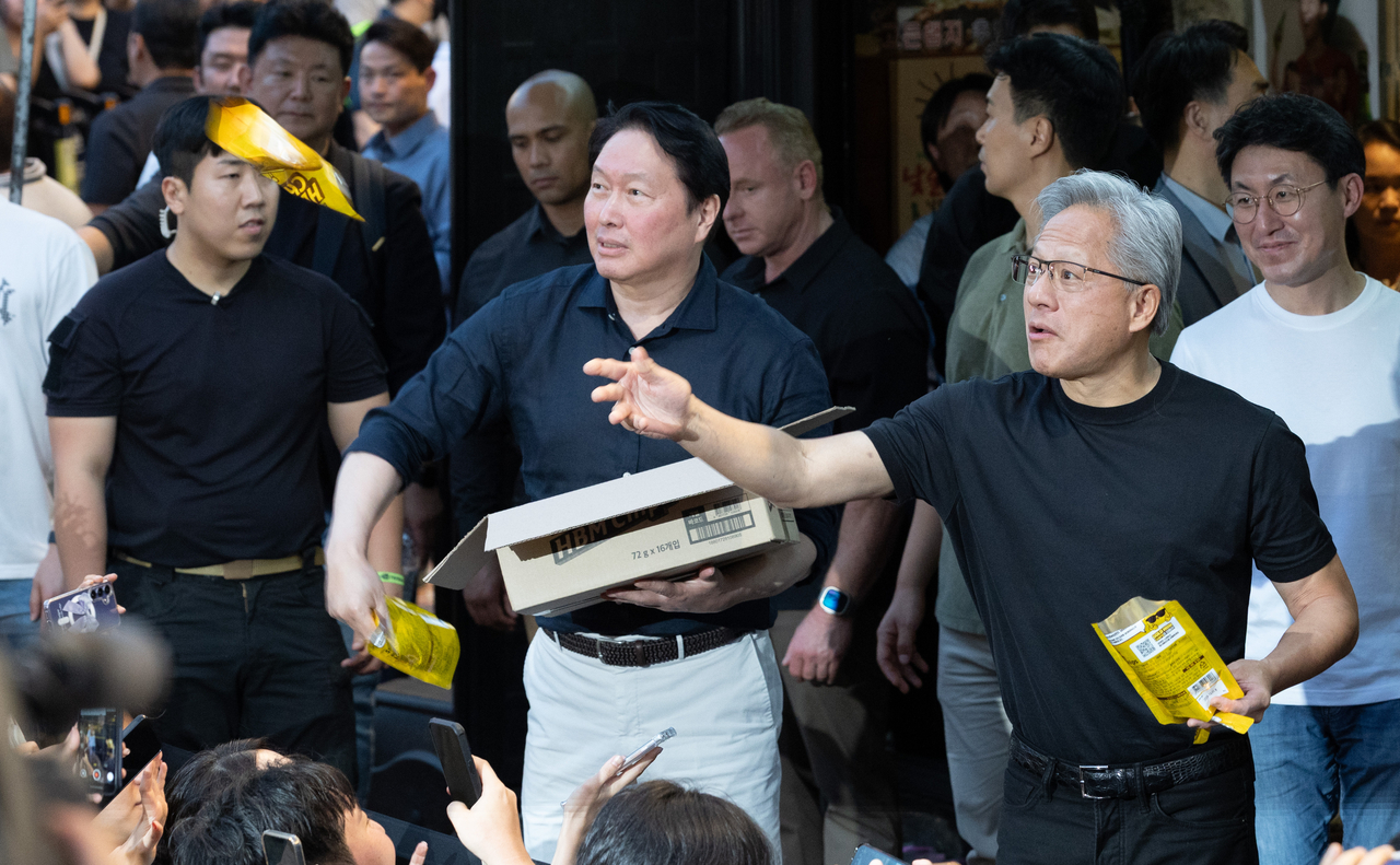 Jensen Huang, CEO of Nvidia, hands out an HBM chip with SK Group Chairman Chey Tae-won at a restaurant near Hongdae in Mapo-gu, Seoul, Friday. (Yoon Chang-bin/The Korea Herald)