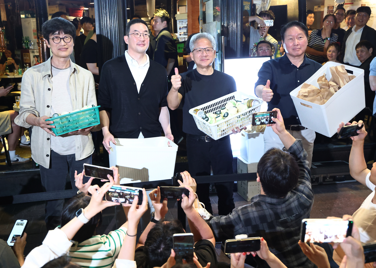 From left: Naver Chair Lee Hae-jin, LG Group Chair Koo Kwang-mo, Nvidia CEO Jensen Huang and SK Group Chair Chey Tae-won hand out snacks to people gathered outside a pork belly restaurant in Hongdae, Seoul, on Friday. (Pool Photo via Yonhap)