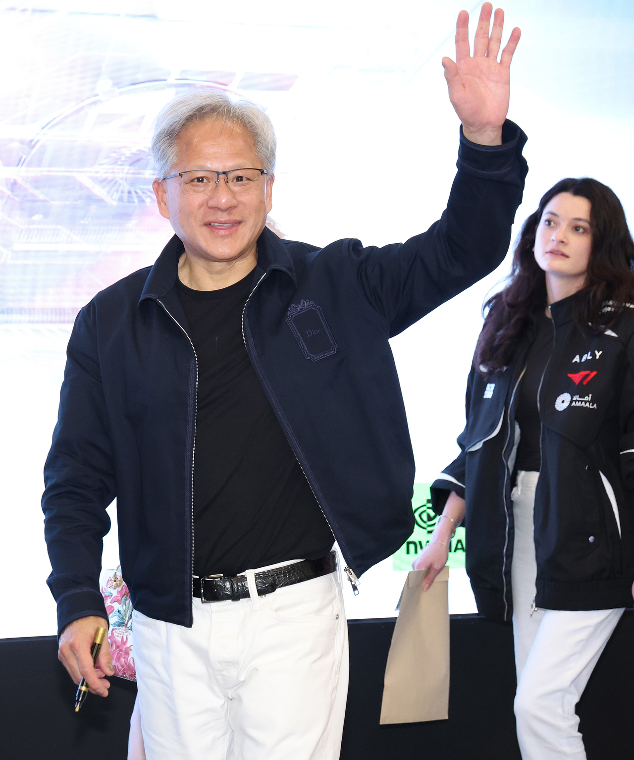 Nvidia CEO Jensen Huang waves as he leaves the T1 Base Camp in Mapo District, Seoul, on Friday after a visit. Behind him is his daughter, Madison Huang. The father and daughter wore similar looks, both pairing jackets with white jeans, toned down with black T-shirts underneath. (Yonhap)