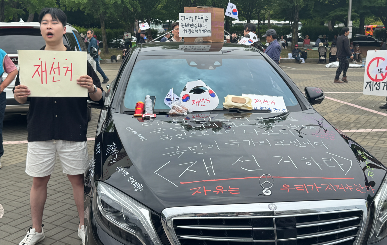 Baek Seung-tae, 25, stands beside his car bearing messages calling for a rerun of the recent local elections in Jamsil-dong, southern Seoul, Sunday. (Cha Min-jung/The Korea Herald)