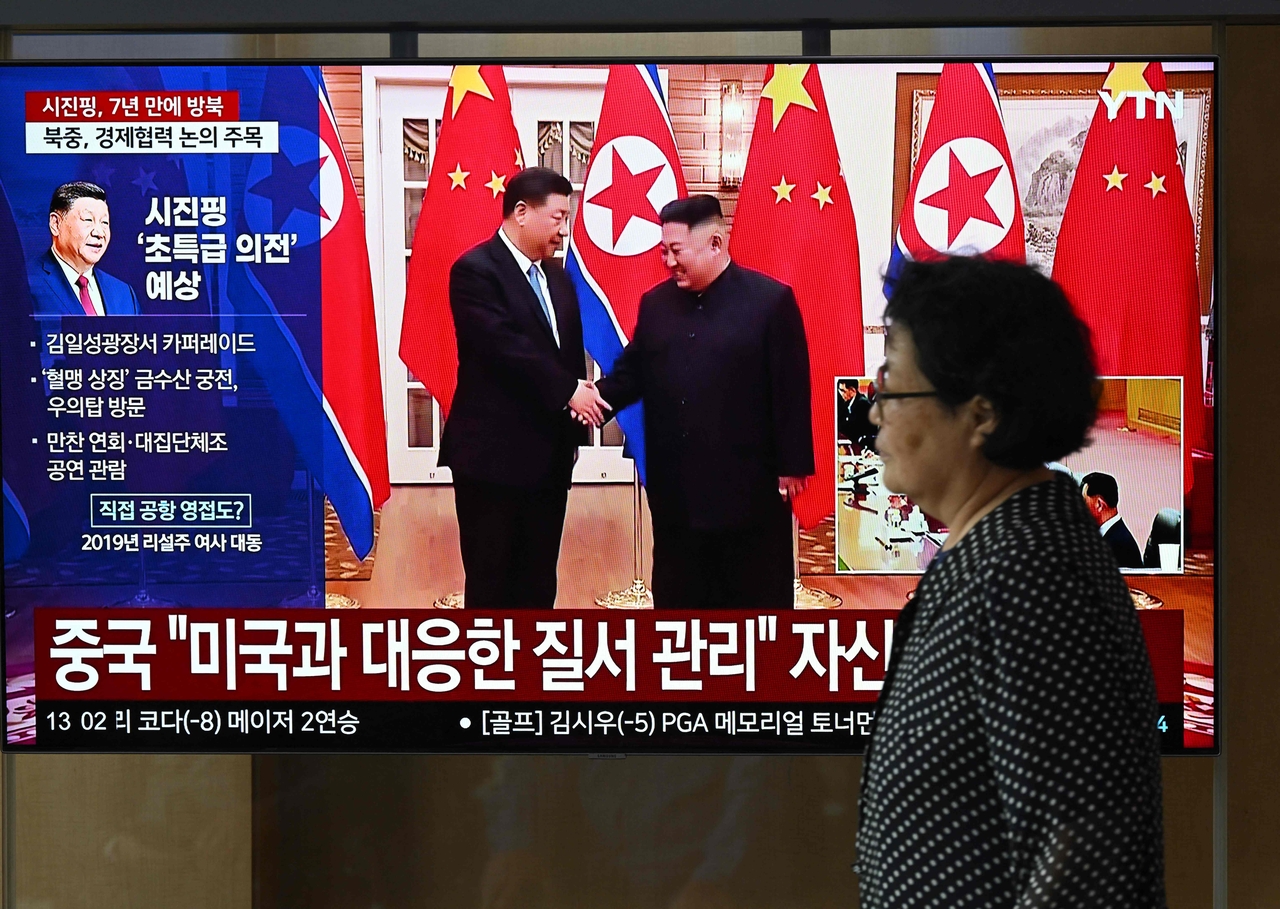 A woman walks past a television screen showing a news broadcast with file footage of the 2019 meeting between China's President Xi Jinping and North Korean leader Kim Jong-un, at a train station in Seoul on Monday. (AFP-Yonhap)