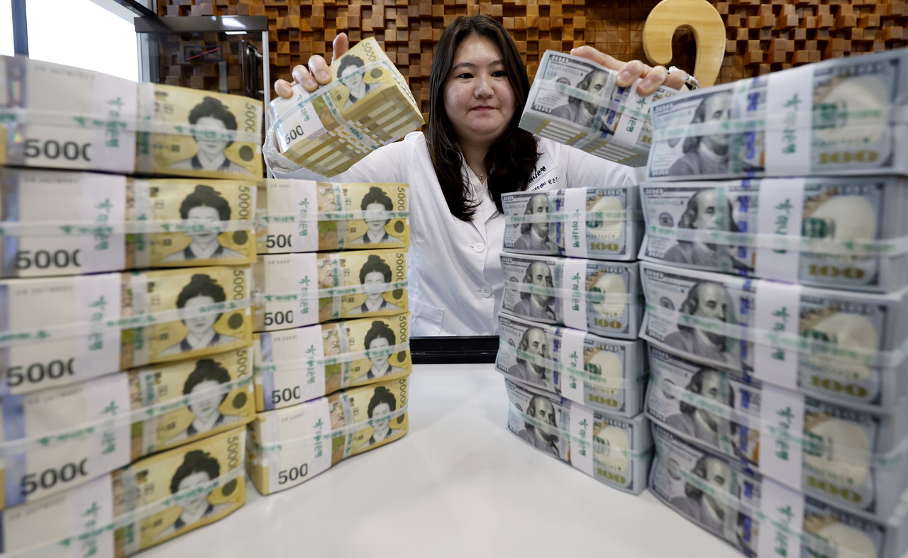 A Hana Bank employee holds stacks Korean and US currency at the lender’s headquarters in central Seoul on June 4. (Newsis)
