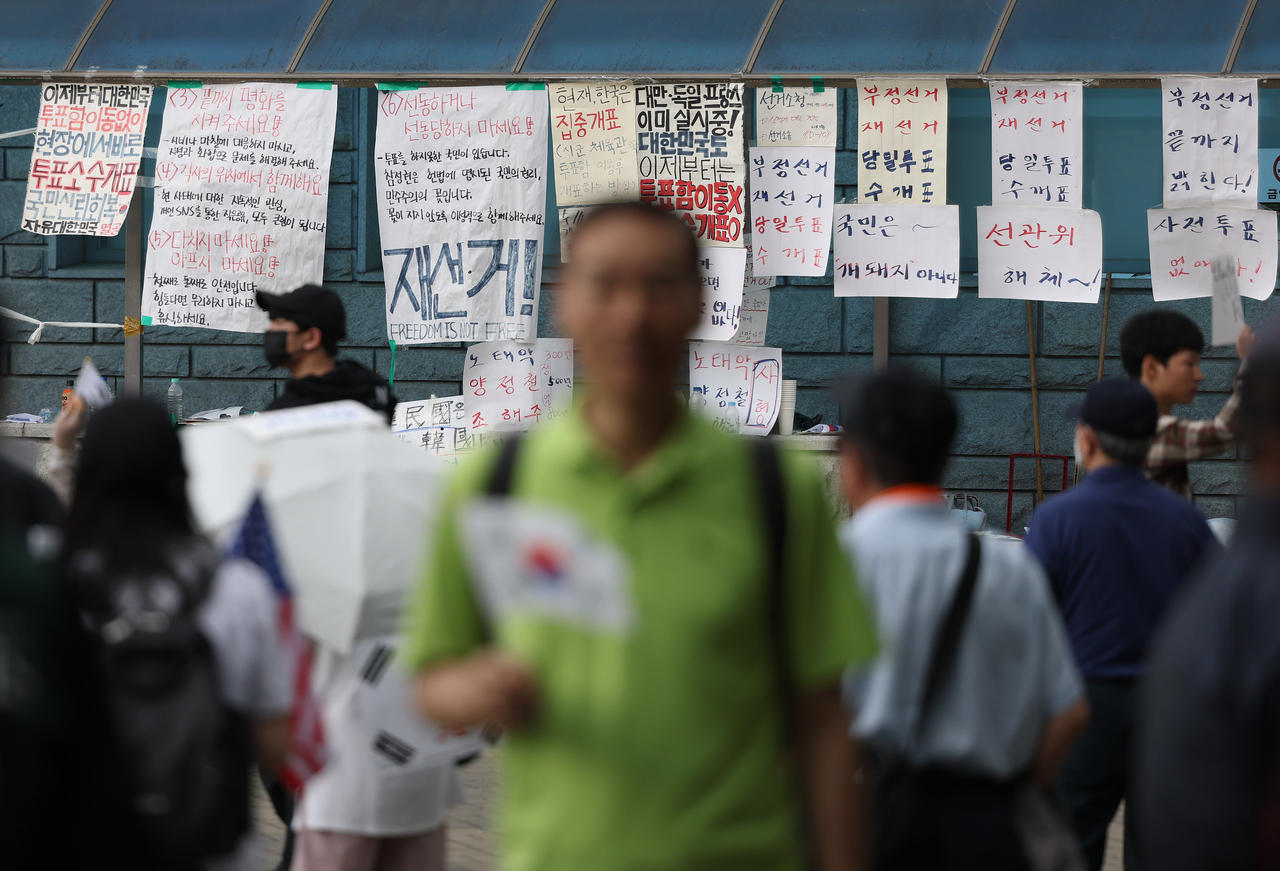 A protester holds a national flag in front of messages calling for a revote of the June 3 local elections outside the Olympic Handball Gymnasium in Seoul on Wednesday. (Yonhap)