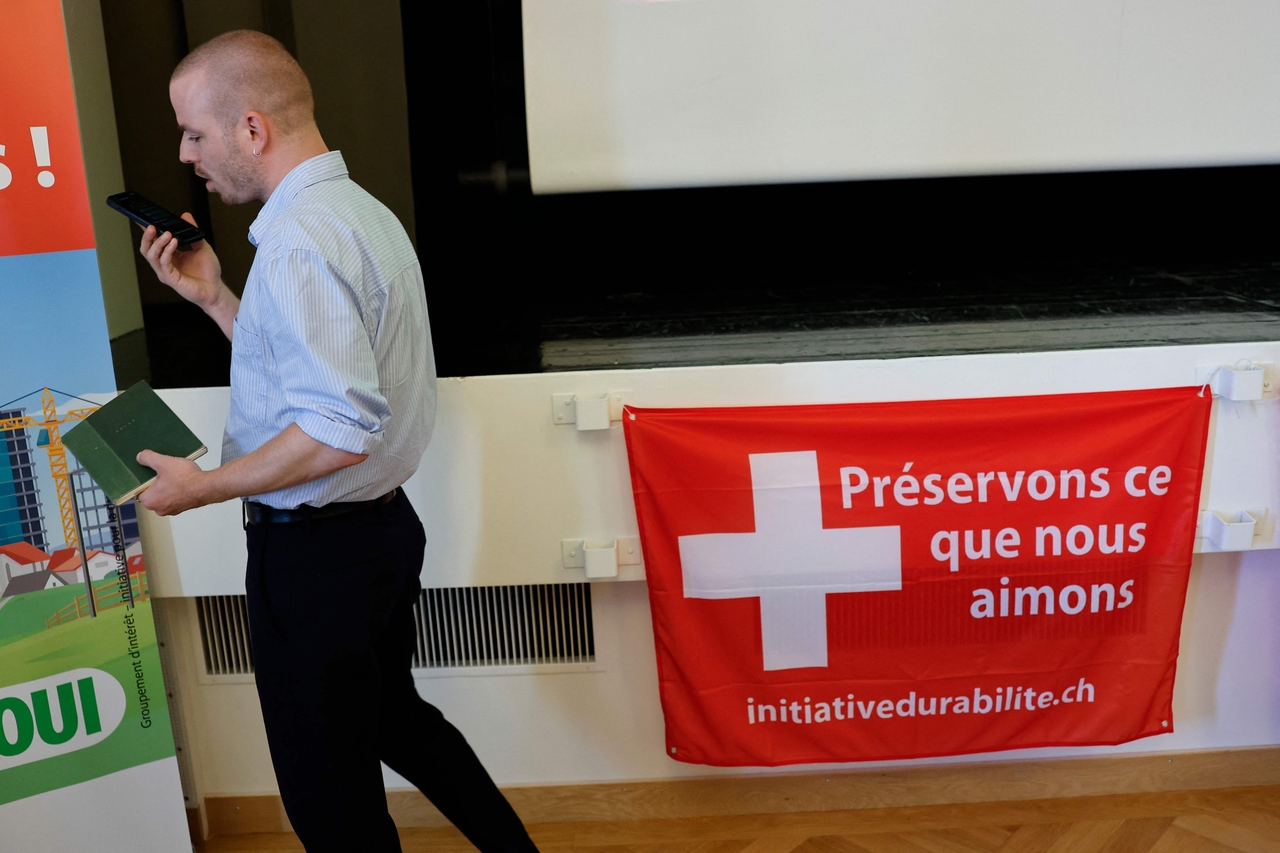 A man speaks on his phone as he walks past a flag reading "Let's preserve what we love" as the Swiss vote on a divisive anti-immigration proposal to cap the country's population and another referendum on restricting access to conscientious objection to military service, in Aarberg on June 14, 2026. (Photo by STEFAN WERMUTH / AFP)