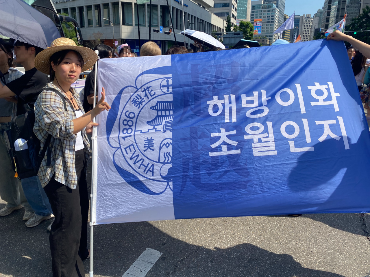 A student of Ewha Womans University poses during the 2026 Seoul Queer Parade in central Seoul on Saturday, holding a flag representing her university. (Lim Jae-seong/The Korea Herald)