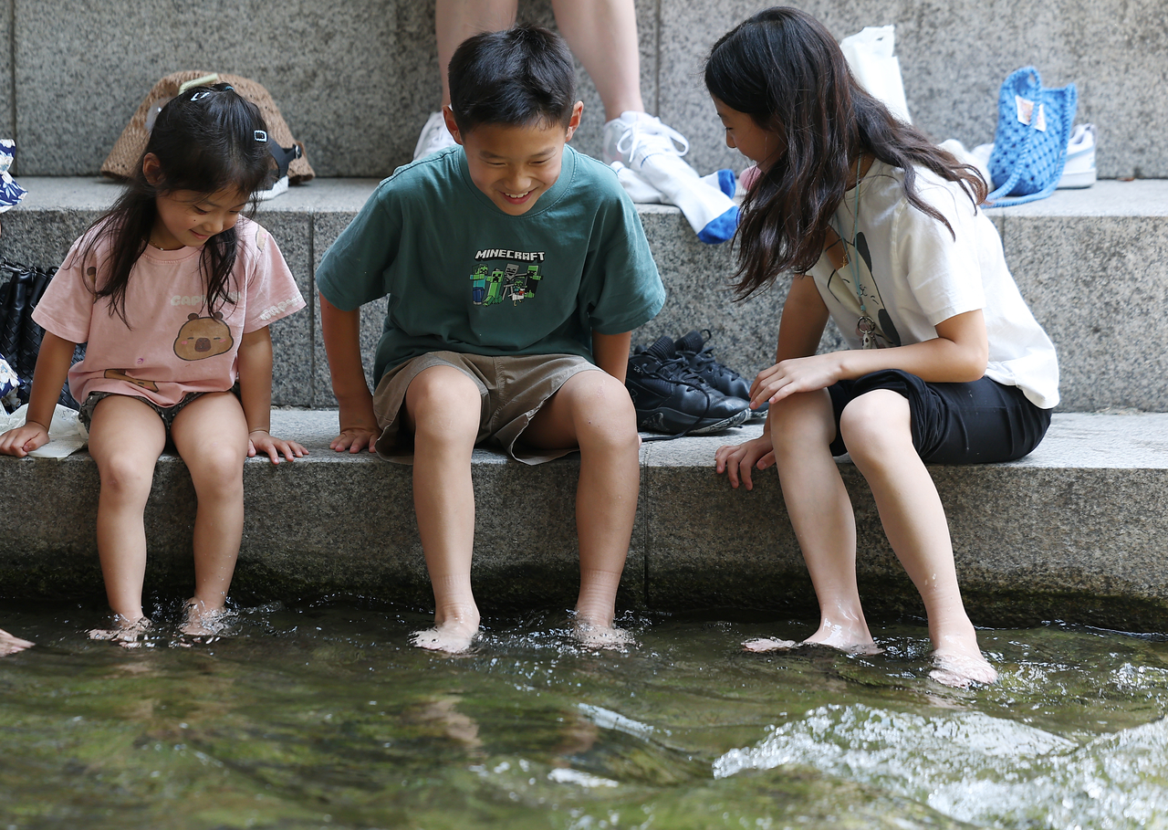 A family of foreign visitors cools off at Cheonggye Stream in Seoul as daytime temperatures reached 33 C on Tuesday. (Yonhap)