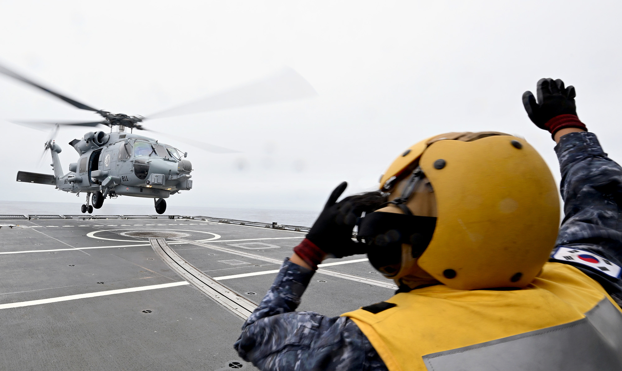 A Navy serviceman signals to an approaching MH-60R helicopter aboard the destroyer Chungmugong Yi Sun-sin during a drill in waters off the southern coast on Thursday. (Republic of Korea Navy)