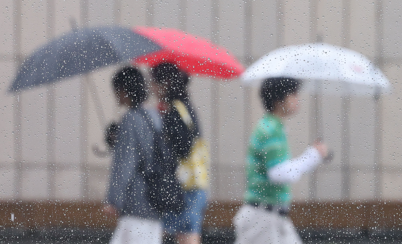 Pedestrians walk through the rain with umbrellas in central Seoul on Saturday. (Yonhap)