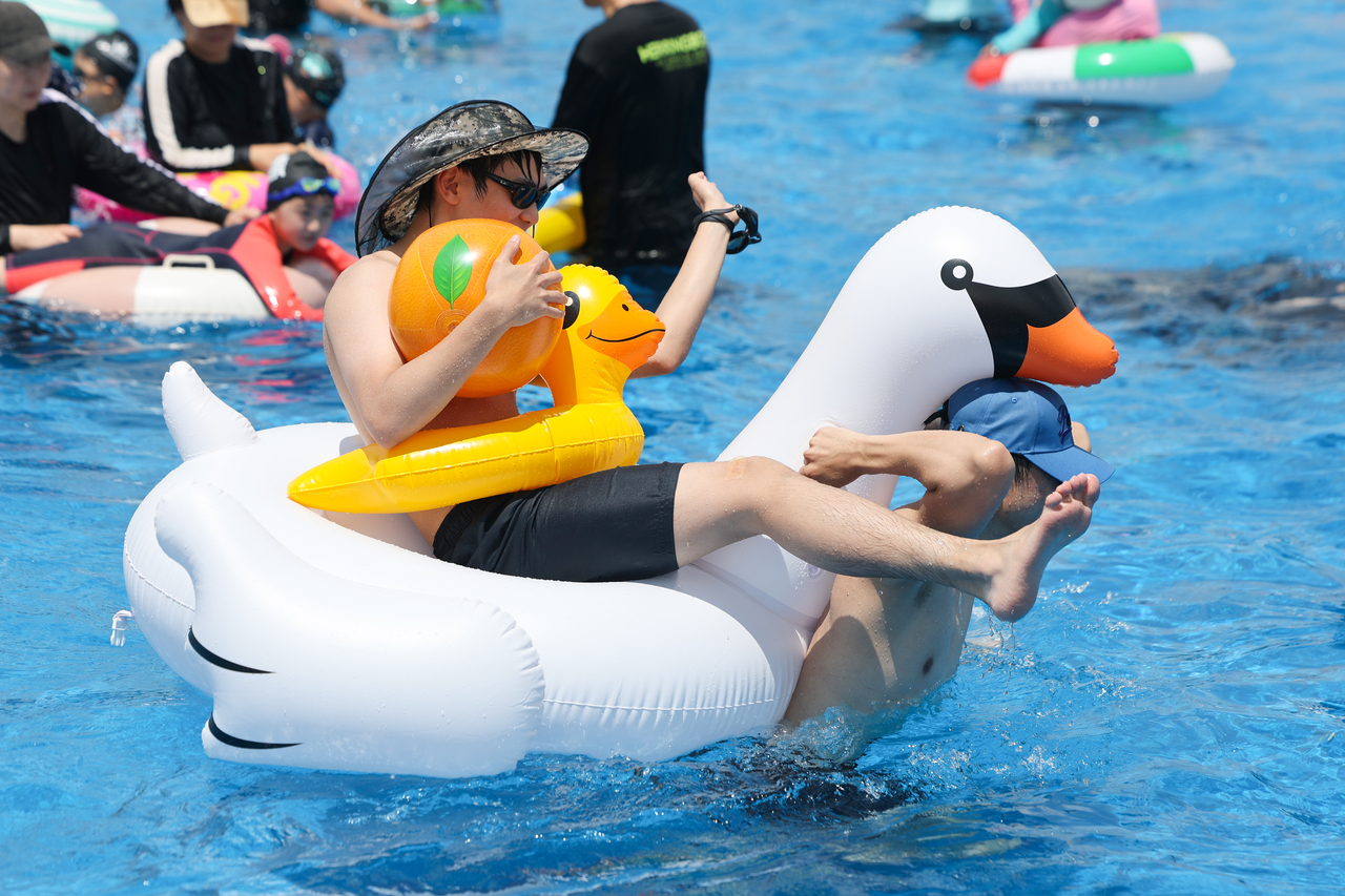 A man carries an inflatable swan carrying another man wearing a duck-shaped floatie and carrying an inflatable orange at Yeouido Hangang Park on Sunday. (Yonhap)
