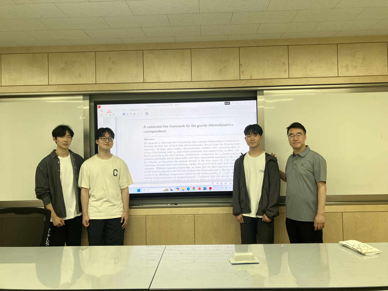 From left: Seoul Science High School students Ahn Geon-woo, Jang Geun-young and Bae I-jin and physics teacher Kwon Yong-joon pose for a photo in front of a projection of their paper published in the International Journal of Modern Physics D. (Seoul Science High School)