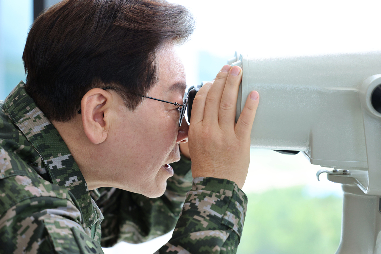 President Lee Jae Myung uses binoculars to look at the North Korean side of the Demilitarized Zone from an observatory on Yeonpyeong Island near the Northern Limit Line, the de facto sea border with North Korea in the Yellow Sea, on Wednesday, as he visits a Marine Corps unit on the island to mark the 76th anniversary the next day of the outbreak of the 1950-53 Korean War. (Pool photo via Yonhap)