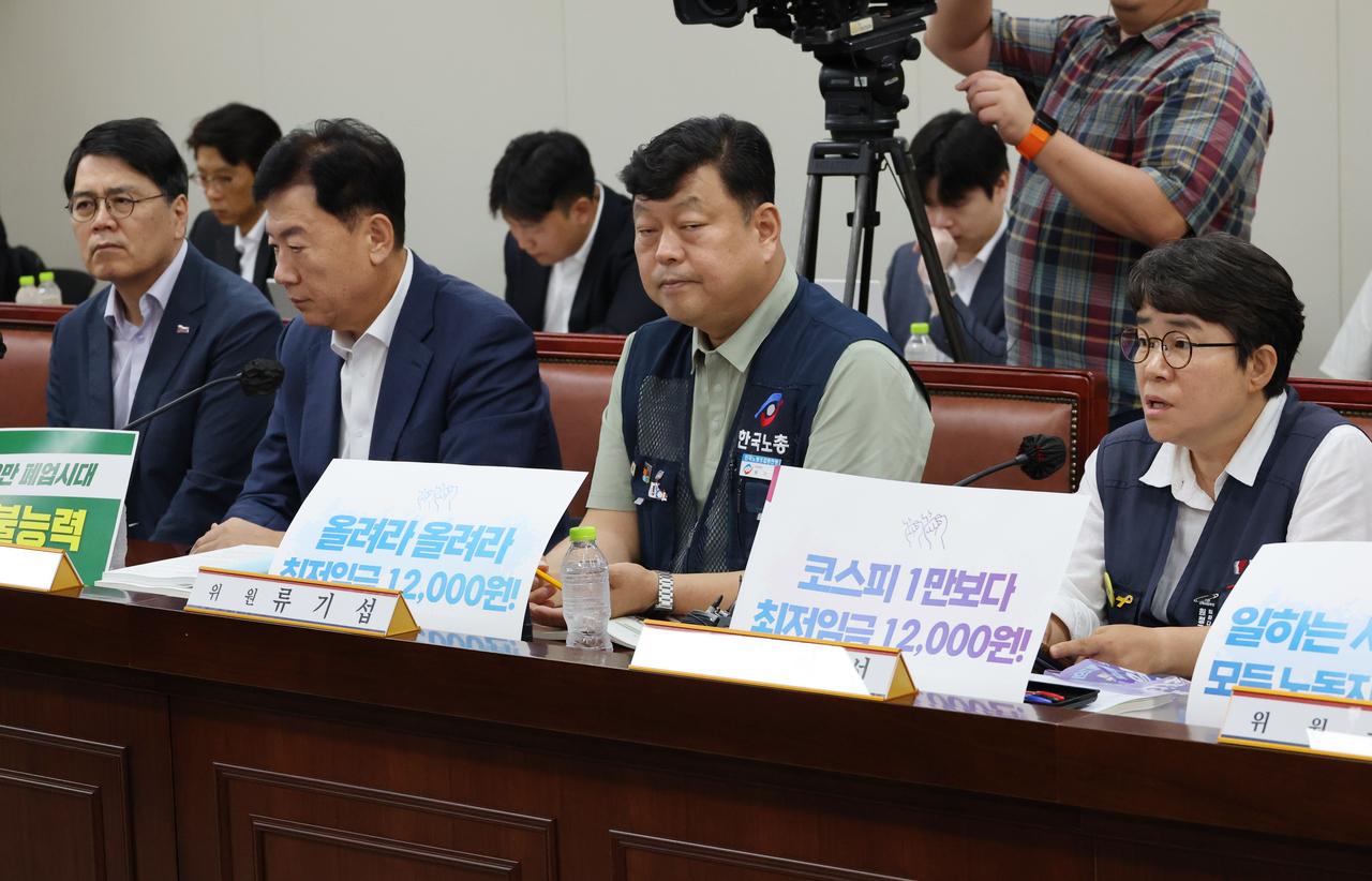 Lee Mi-sun, a worker representative on the Minimum Wage Commission and vice chairwoman of the Korean Confederation of Trade Unions, holds up a sign reading "12,000 won (about $8) minimum wage over a Kospi 10,000!" during the commission's eighth plenary session at the Government Sejong Building on Tuesday. [Yonhap]