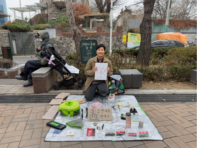 Chun Geun-sung  displays everyday items on a mat in a park near Seoul Station as part of his public art project "My Homeless Neighbors," in which he invited people to purchase the items with drawings instead of money in 2023. (Hysterian, Chun Geun-sung)