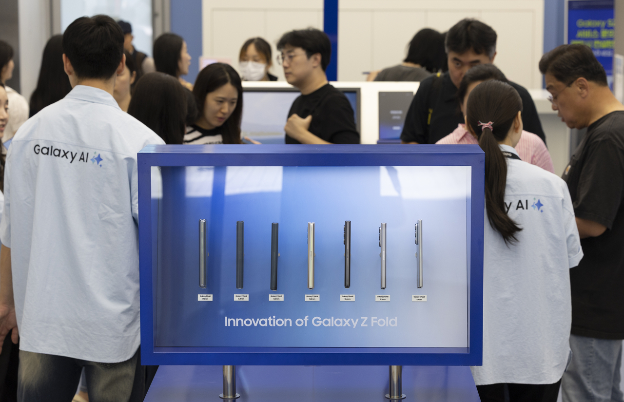 Shoppers browse seven Galaxy Z Fold generations, lined up by thickness, at a Samsung store in Seoul during the Fold 7 launch in July 2025. The latest model has shrunk to 8.9mm folded, roughly half the original and close to an ordinary phone. (Newsis)