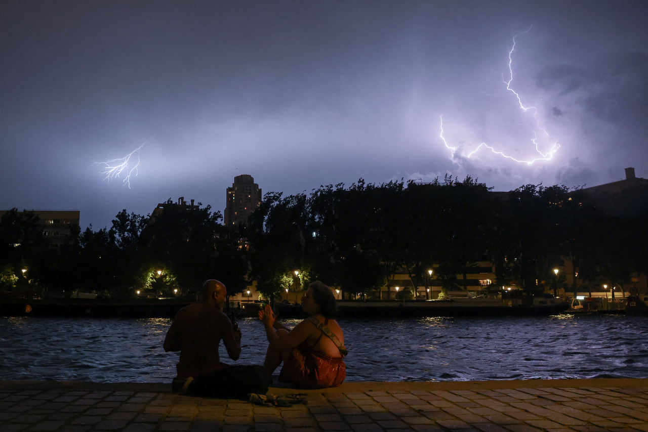 People sit on the banks of the Bassin de la Villette during a storm, as lightning strikes behind them amid a heatwave in Paris, France, Saturday. (Reuters-Yonhap)