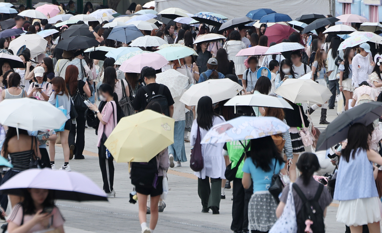 Concertgoers wait under umbrellas outside the Olympic Gymnastics Arena in Songpa-gu, Seoul, on Sunday, as a heat wave continues. (Yonhap)