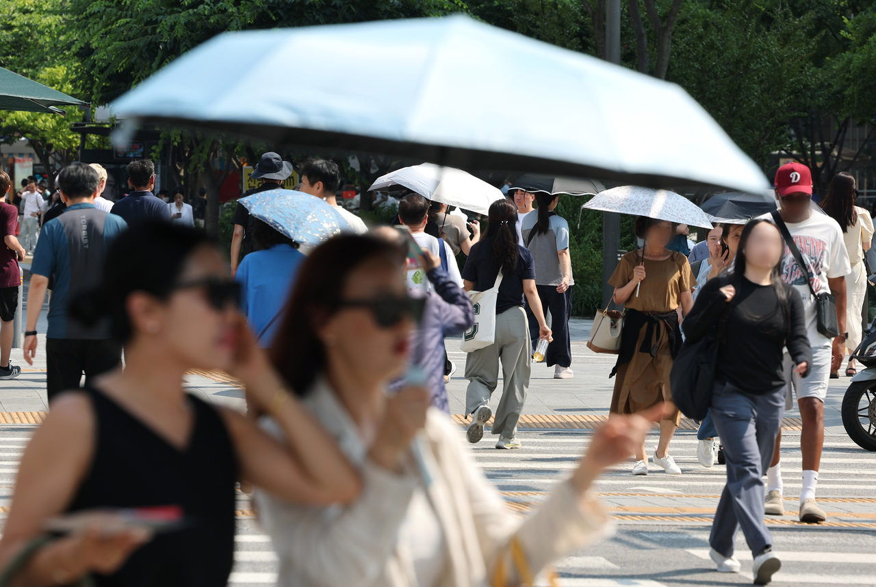 Pedestrians carry parasols as they cross a street in Gwanghwamun, Seoul on June 18. (Yonhap)