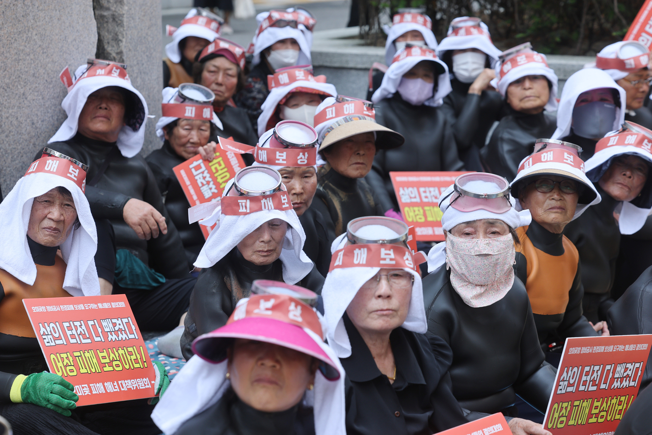 Protesting haenyeo are seen holding banners that read "Our livelihoods have been taken away. Compensate for the damage" and wearing headbands with the same message in front of Ssangyong Engineering & Construction's headquarters in Seoul's Songpa District on Monday. (Yonhap)