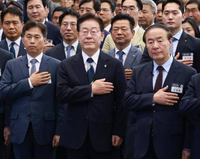President Lee Jae Myung (center), Samsung Electronics Vice Chairman Jun Young-hyun (right) and SK hynix CEO Kwak Noh-jung stand for the national pledge during a public briefing at Kimdaejung Convention Center in Gwangju on Tuesday. (Yonhap)