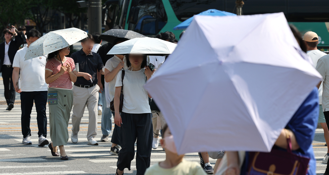 Pedestrians carrying parasols cross a street near Gwanghwamun Square in central Seoul on June18. (Yonhap)
