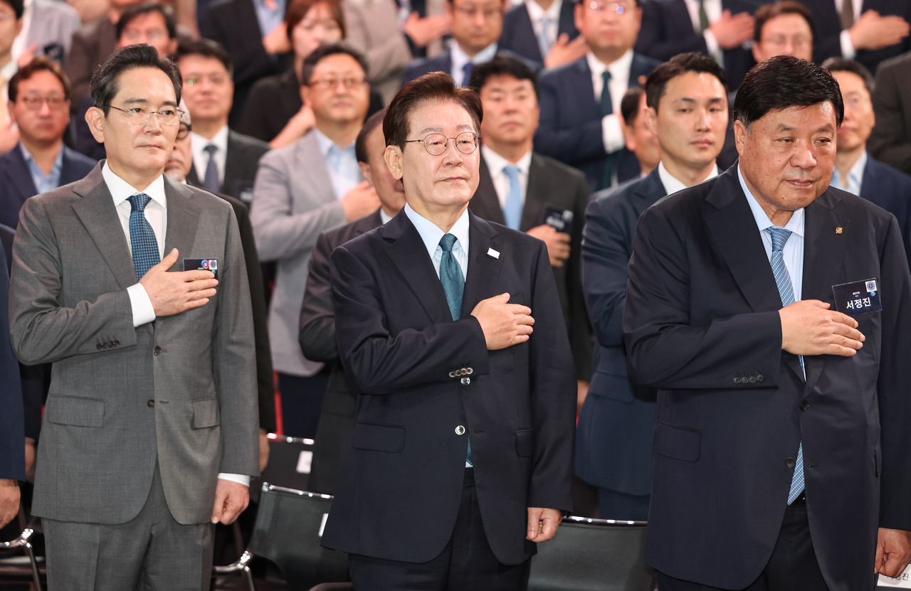 President Lee Jae Myung (center), Samsung Electronics Chairman Lee Jae-yong (left) and Celltrion Chairman Seo Jung-jin salute the national flag during a public briefing on the development vision for advanced industries in the Chungcheong region in Asan, South Chungcheong Province, Thursday. (Pool photo via Yonhap)