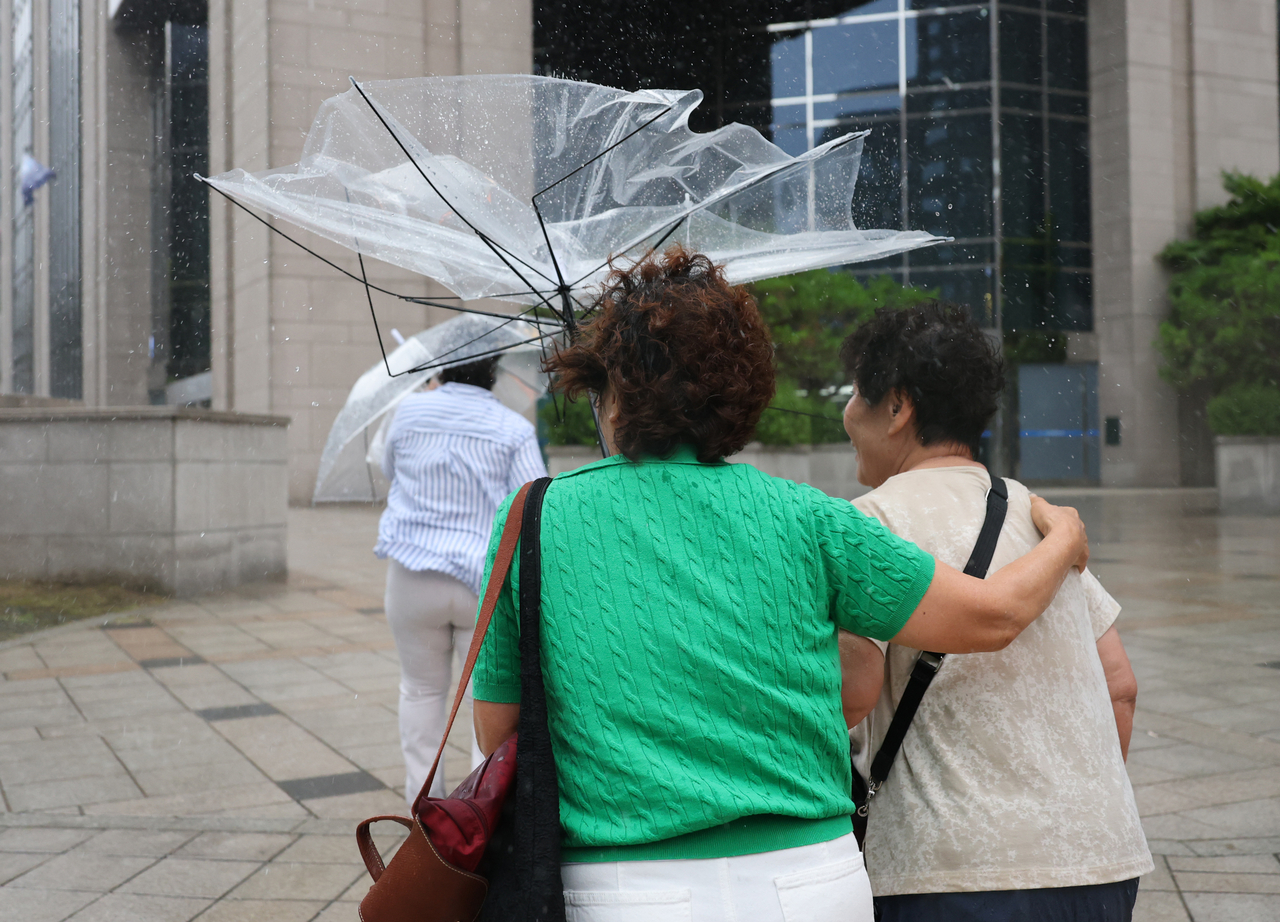 Rain and strong winds flip a passenger's umbrella near Myeong-dong in Seoul on June 19. (Yonhap)